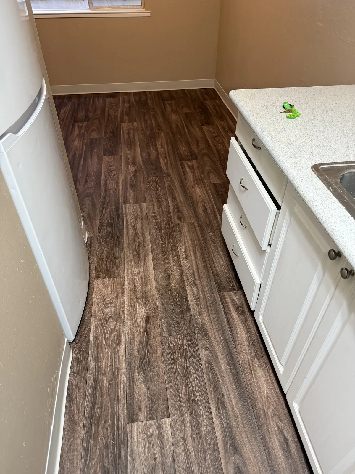 Completed dark wood-look flooring between white kitchen cabinets at Woodland Park